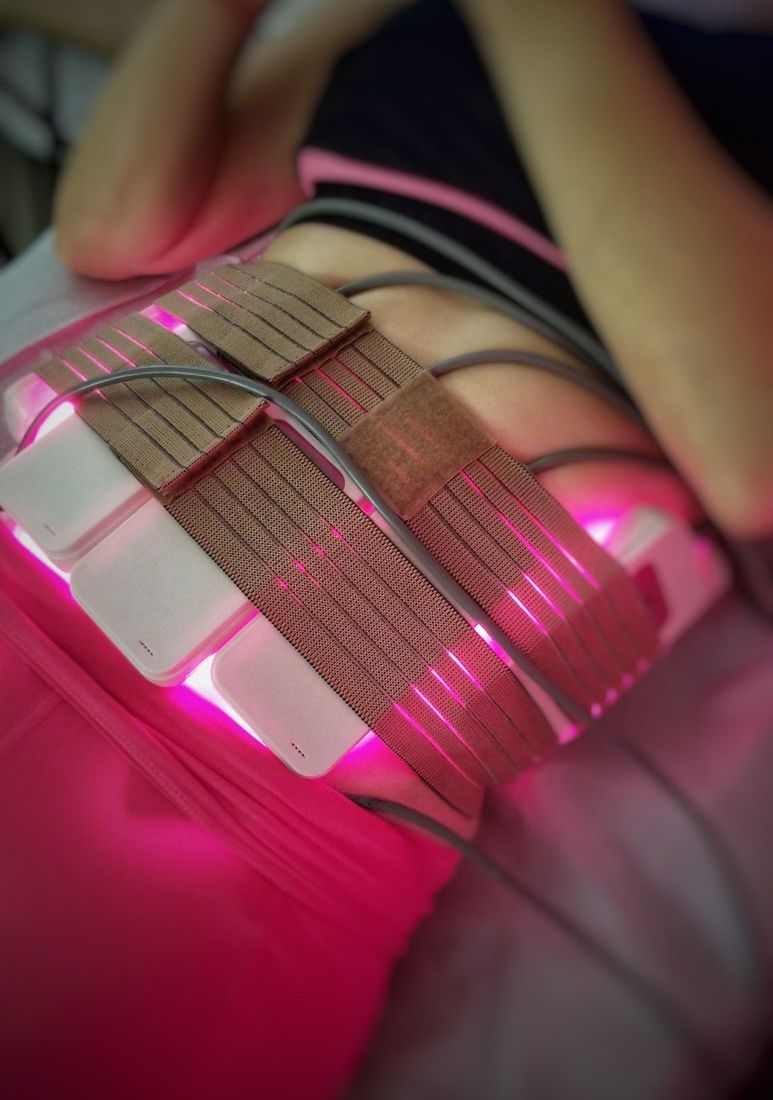 Des plaques de lipolaser à lumière rose fixées sur le ventre par des sangles.