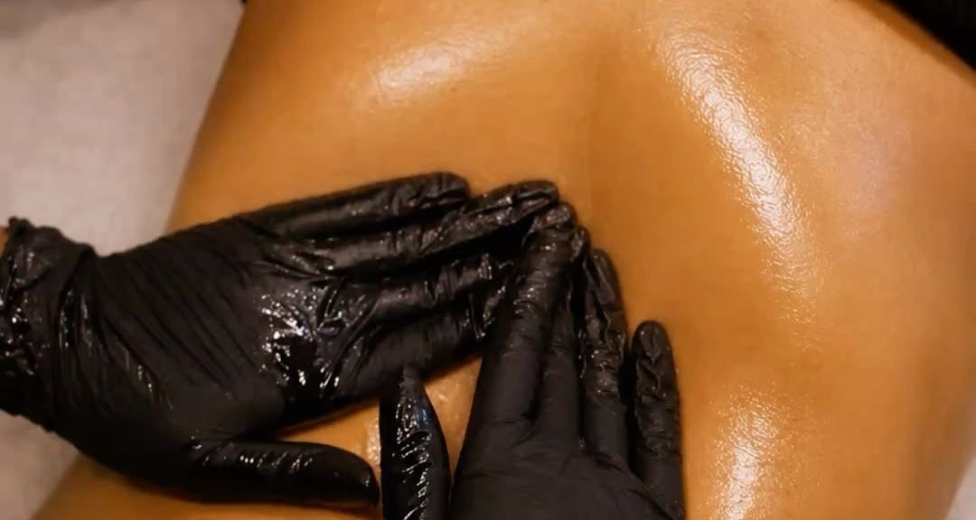 Des mains gantées massent un dos huilé.