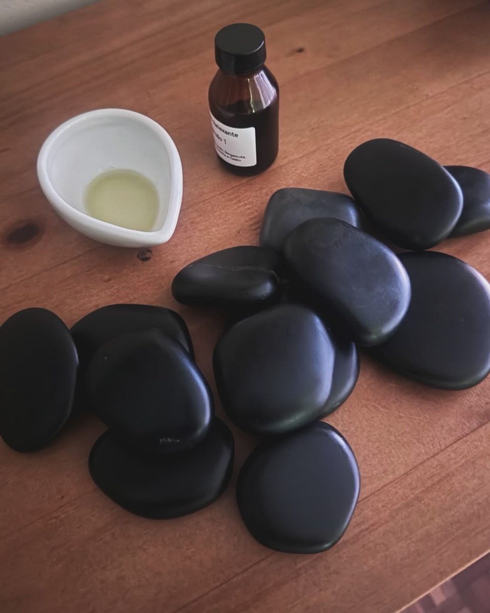 Des pierres de basalte noires, un flacon d'huile et une coupelle sur une table en bois.