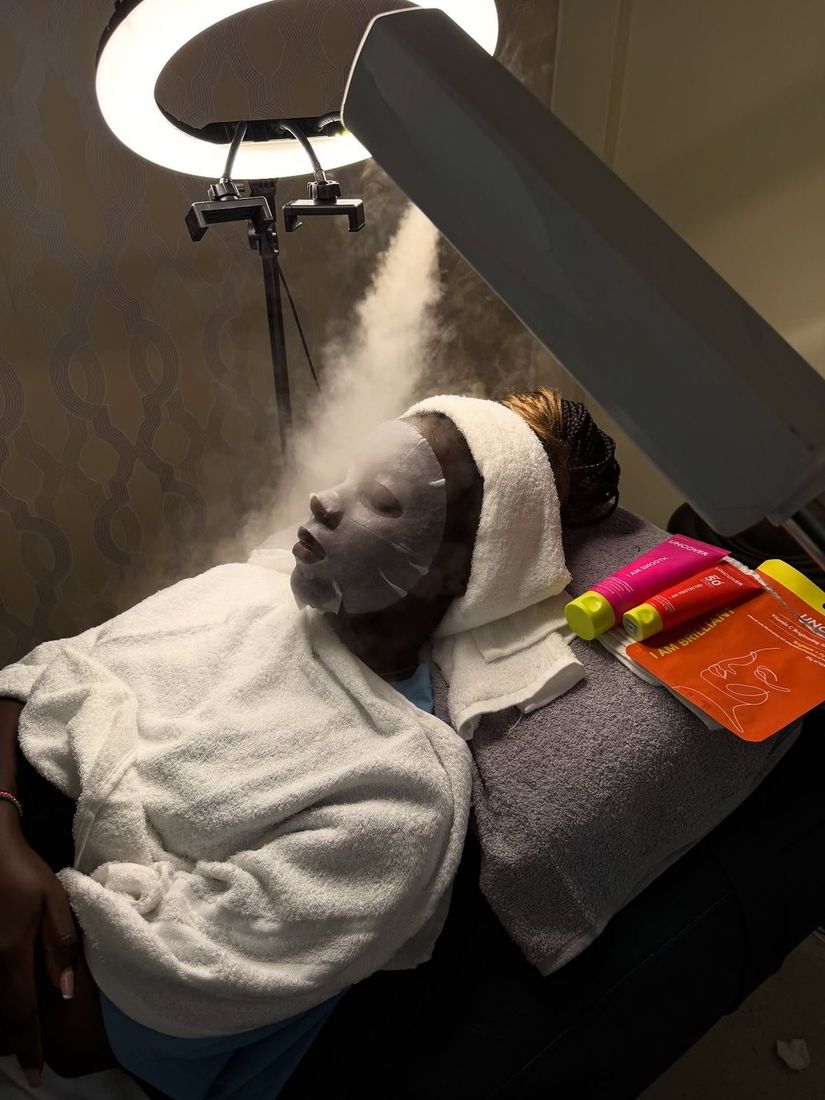 Une cliente en peignoir sous un jet de vapeur et une lampe circulaire.