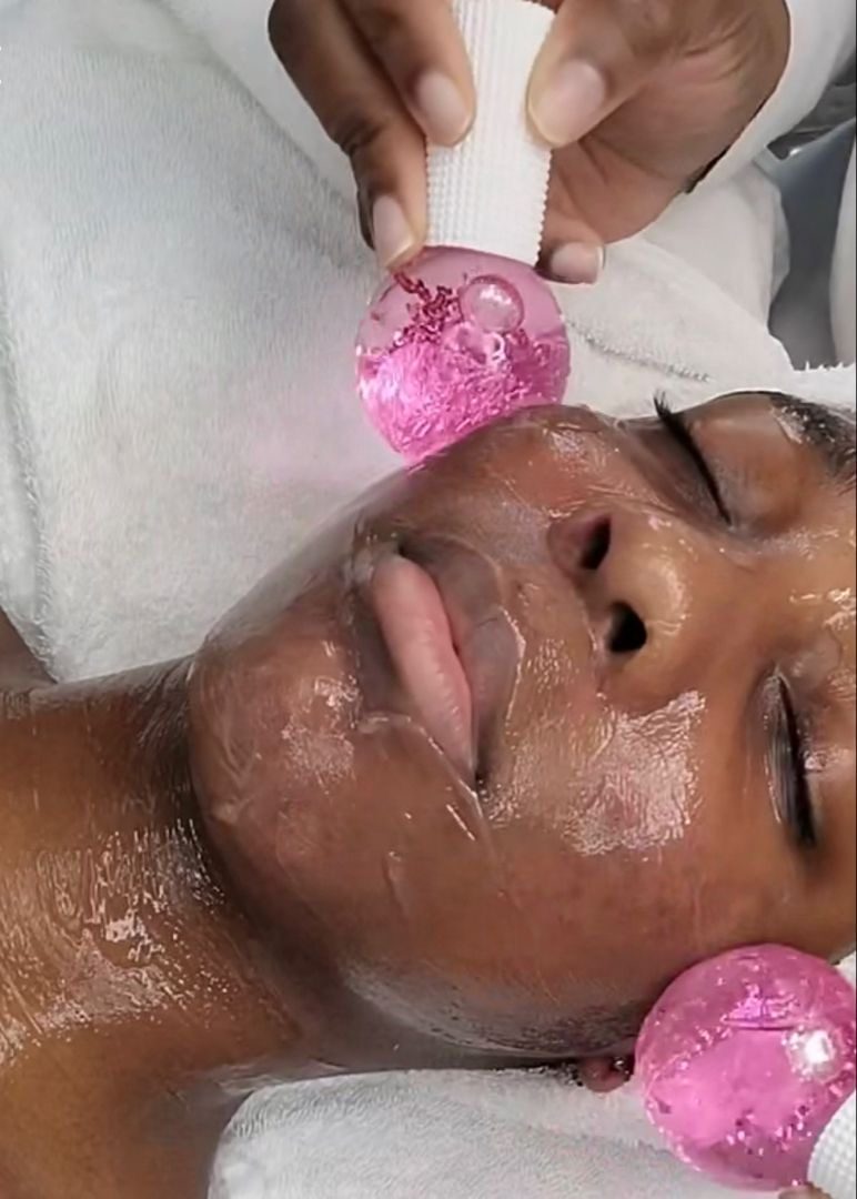 Un globe de massage rose glissé le long de la mâchoire d'une cliente.